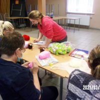 Uczestniczki spotkania siedzą przy stołach i szydełkują.