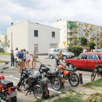 Uczestnicy spotkania stojący na parkingu przed biblioteką rozmawiają między sobą.