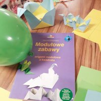 Zdjęcie książki zatytułowanej "Modułowe zabawy czyli origami modułowe z kwadratu", książka leży na stole pomiędzy wykonanymi koszyczkami.