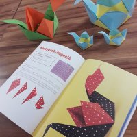 Na zdjęciu widać książkę do origami otwartą na jednej ze stron, powyżej książki leżą wykonane metodą origami koszyczki.