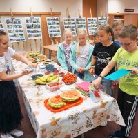 Dzieci ustawione w kolejce biorą przybory kuchenne takie jak deski do krojenia i nożyki.