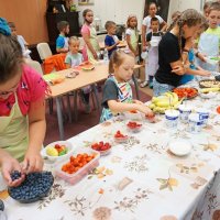 Dzieci biorą składniki do przyrządzenia zdrowych przekąsek, tymi składnikami są: arbuzy, truskawki, borówki, banany i daktyle.