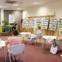 Na zdjęciu widać trzy uczestniczki spotkania, prowadzącą oraz zaproszonego gościa a pod ścianą stoją plansze z wystawianymi fotografiami.