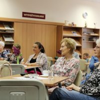 Zdjęcie części publiczności, widać ziedem osób siedzących przy stolikach i słuchających koncertu.