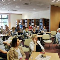 Zdjęcie widowni, na którym widać osoby siedzące przy stolikach z ciastkami i kawą, słuchających opowieści Pana Michała Szulima