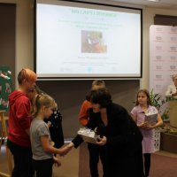 Dyrektor biblioteki wręcza nagrodę dla uczestniczki konkursu fotograficznego.