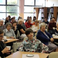 Zdjęcie publiczności, uczestnicy spotkania siedzą przy stolikach i słuchają poezji czytanej przez zaproszonych gości.