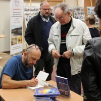 Robert Robb Maciąg składa autograf w książce jednego z widzów.