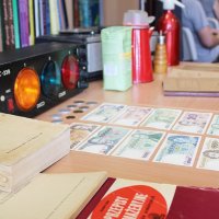 Zdjęcie wystawy przedmiotów z PRL-u, widać książki kucharskie z tamtego okresu, banknoty i oświetlenie dyskotekowe.