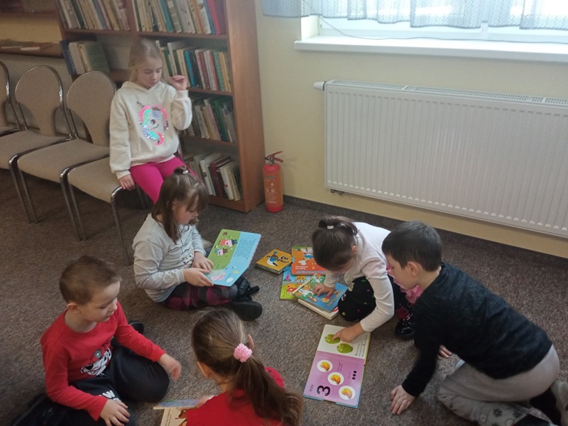 Szóstka dzieci siedzi na podłodze i przegląda książki.