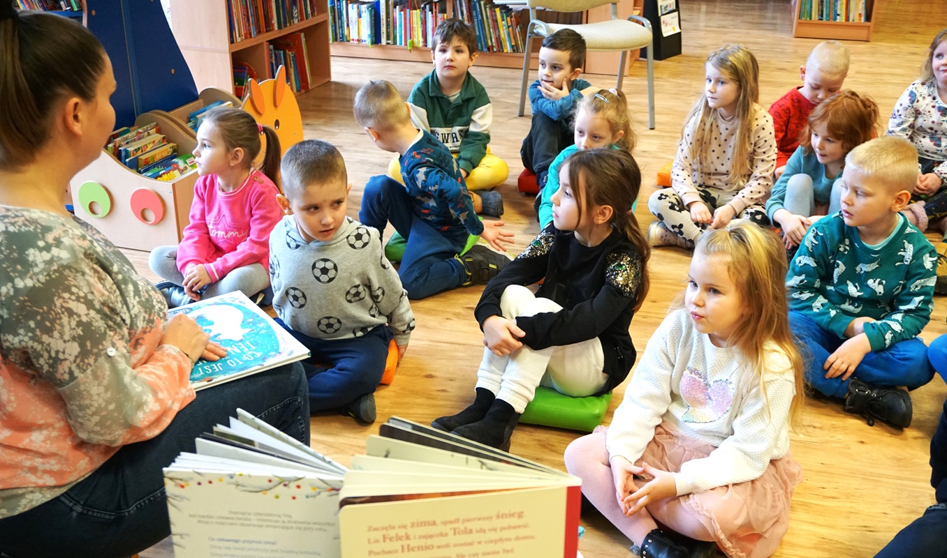 dzieci słuchające bibliotekarki która czyta im ksążkę