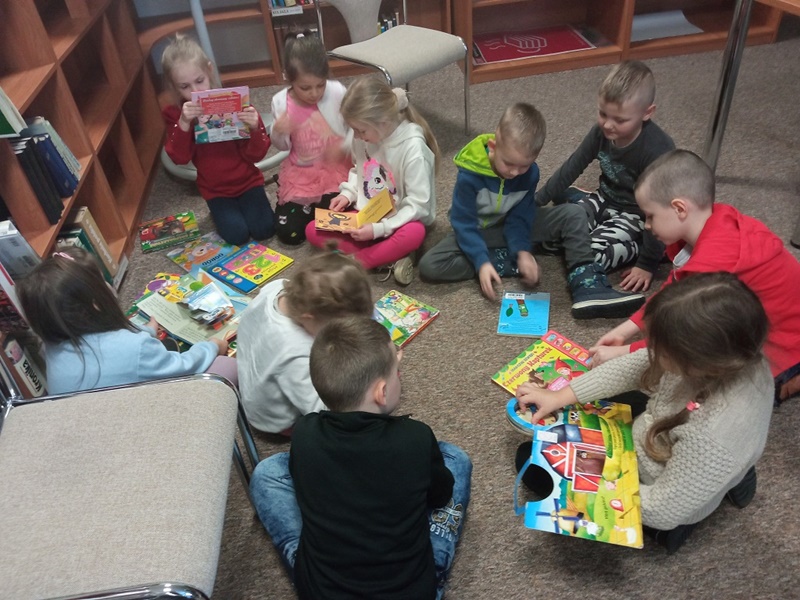 Dziesięcioro dzieci siedzi z książkami na podłodze i je przegląda.