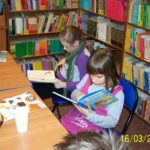 2 dziewczynki siedzą na krzesłach i czytają książki, przed nimi na stołach leżą ciastka, kolorowe czasopisma dla dzieci i jednorazowe kubki