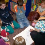 Dzieci wraz z bibliotekarką klęczą na podłodze i rysują na kartce papieru gwiazdę.
