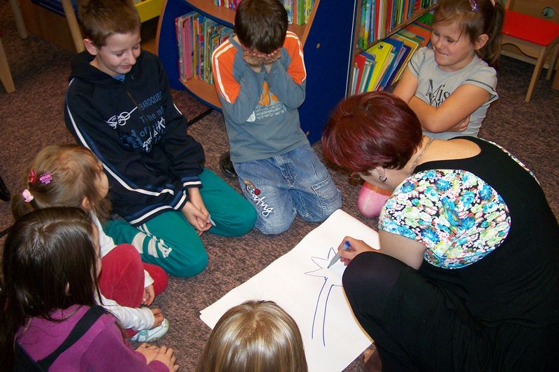 Dzieci wraz z bibliotekarką klęczą na podłodze i rysują na kartce papieru gwiazdę.