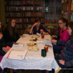 6 dziewczyn siedzących wokół stołu, na stole leżą notatki, książki, talerzyki z ciastkami