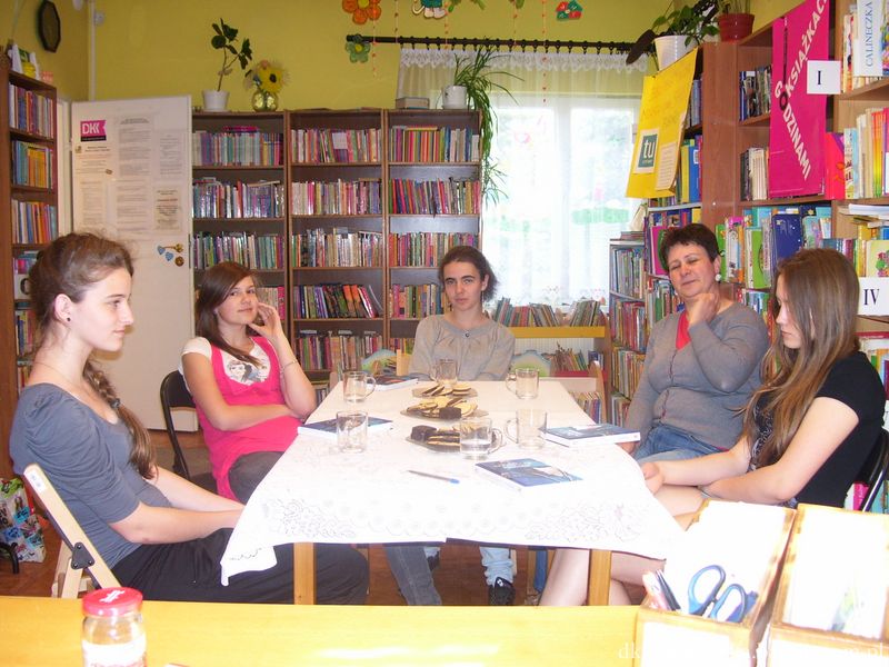 5 osób ( 4 uczestniczki i prowadząca) siedzą przy stole, pzred nimi leżą książki, talerzyki z ciastkami