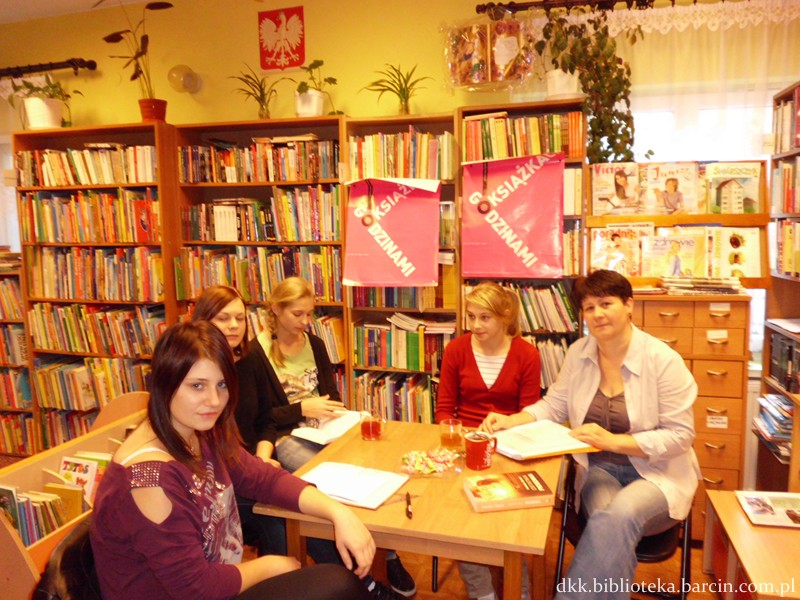 4 czytelniczki i bibliotekarka w czasie spotkania, siedzą wokół kwadratowego stołu, cześć z nich trzyma otwarte ksiażki.
