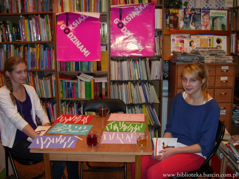 2 dziewczyny siedzące przy stole na którym leżą kolorowe kartki papieru z białymi paskami papieru na wierzchu