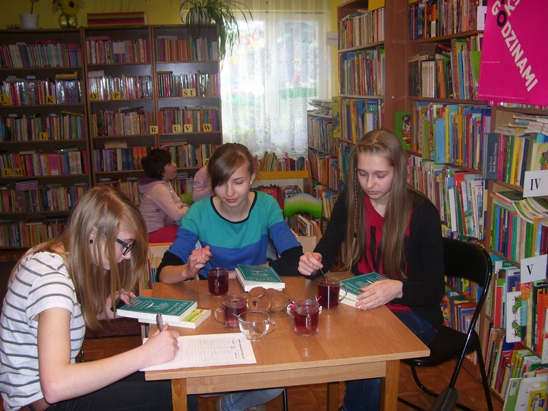 Trzy uczestniczki spotkania siedzą przy stole, przed nimi leżą książki, stoją szklanki z napojami. jedna z uczestniczek notuje coś na kartce papieru