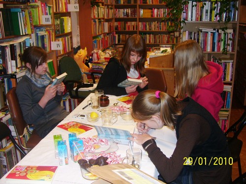 Cztery dziewczyny siedzą przy stole, dwie trzymają w rękach książki, jedna coś zapisuje