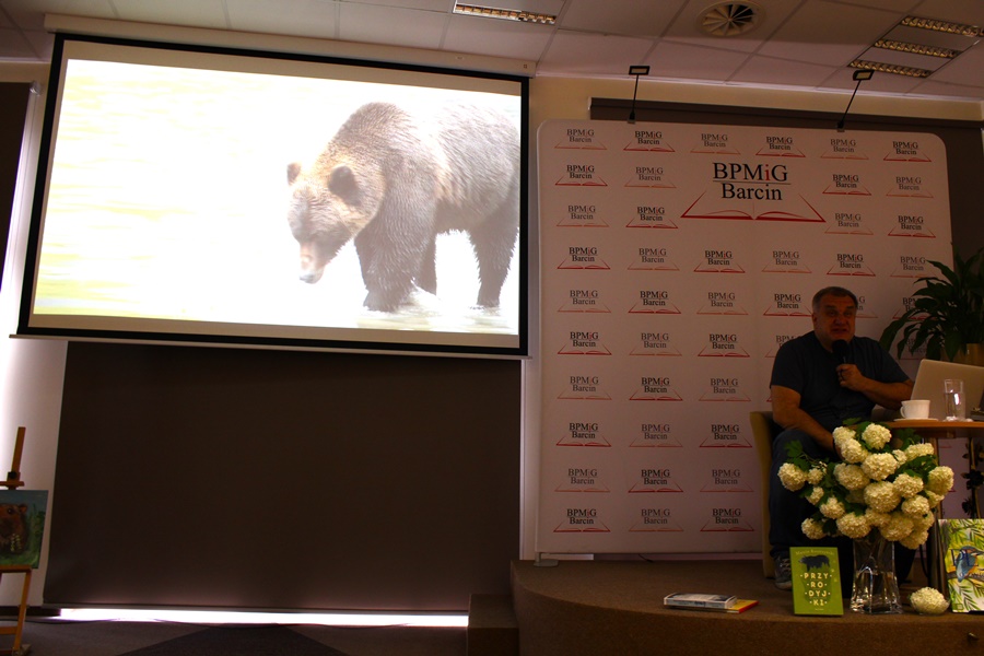 Marcin Kostrzyński siedzi przed komputerem, na ekranie projektora wyświetlane jest zdjęcie niedźwiedzia.