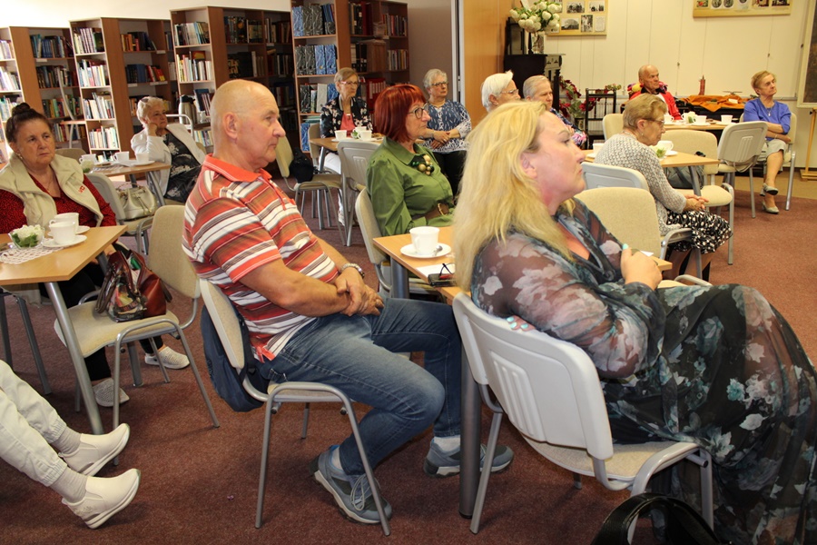 Część gości zebranych na spotkaniu przysłuchuje się rozmowie bibliotekarki prowadzącej spotkanie i Michała Wójcika