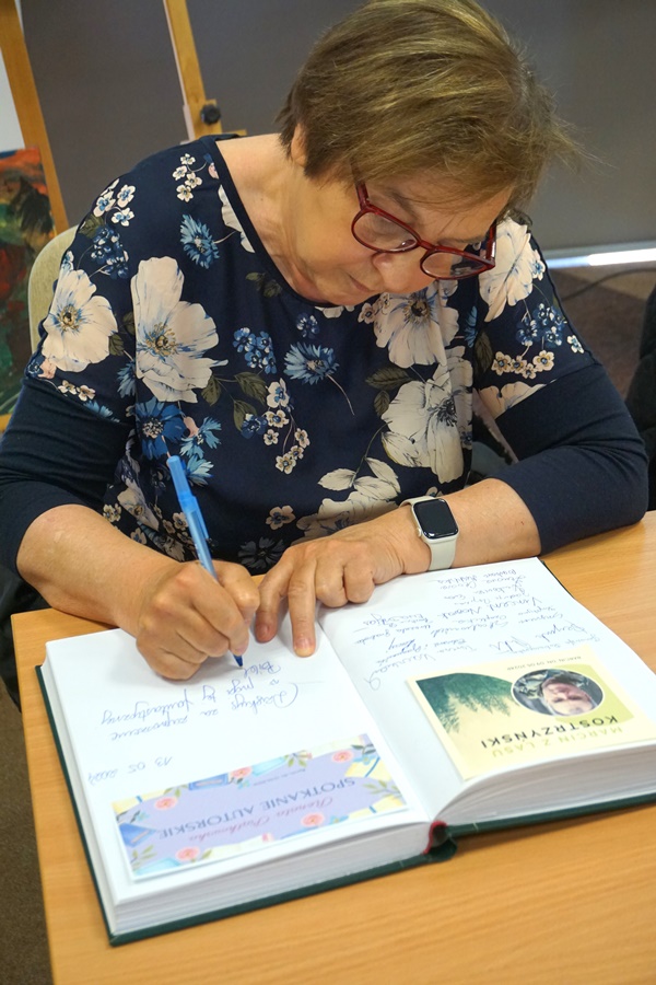 Zaproszona autorka wpisuje się do księgo pamiątkowej ksiąegi w bibliotece.
