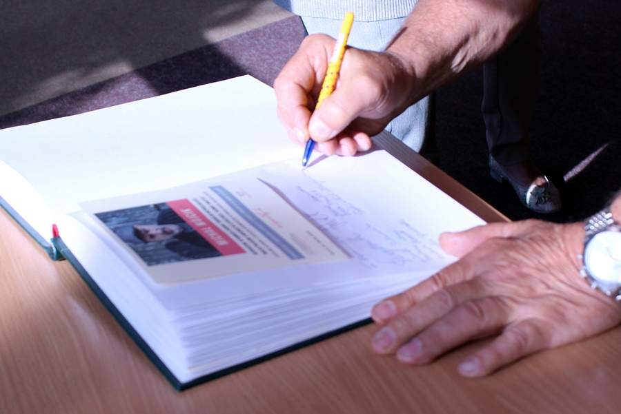 moment gdy jedna z osób wpisuje się do księgi pamiątkowej, widać samą księgę i dłonie trzymające długopis.