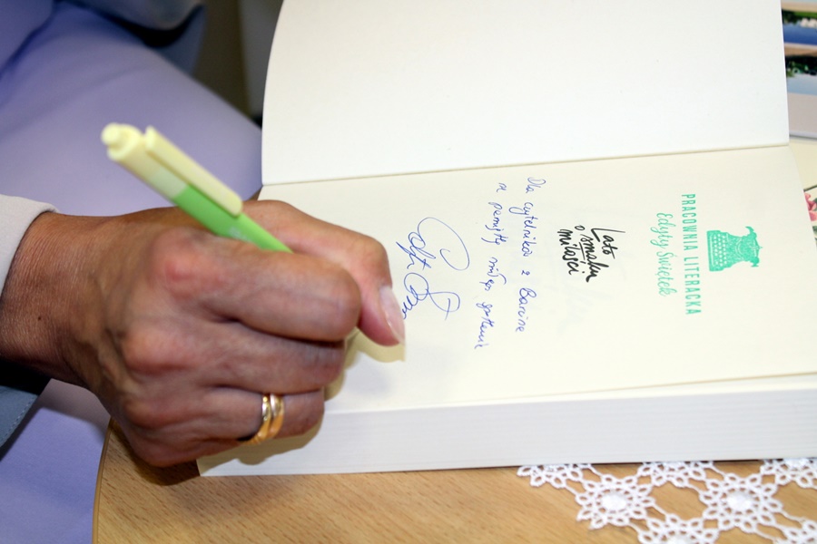 Zbliżenie na podpisywaną książkę, widać dłoń trzymającą długopis, pieczątkę i dedykację złożoną na pierwszej stronie otwartej książki.