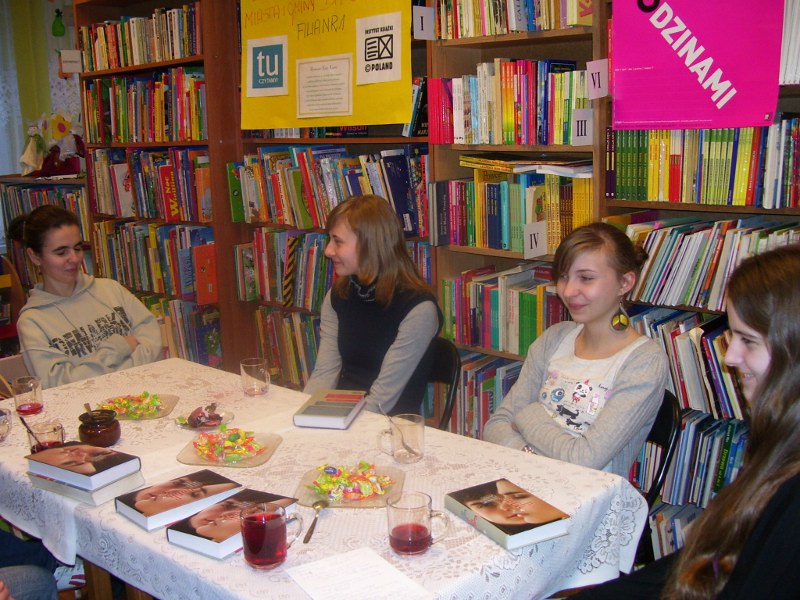 4 dziewczyny biorące udział w spotkaniu siedzą przy stole, uśmiechają się.