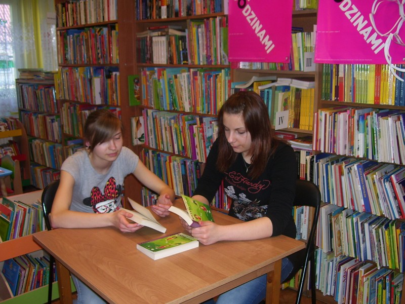 Dwie dziewczyny siedzą przy stole w rękach trzymają książki.