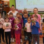 grupowe zdjęcie dzieci biorących udział w warsztatach, razem z dziećmi stoi bibliotekarka, dzieci trzymają doniczki z sadzonkami
