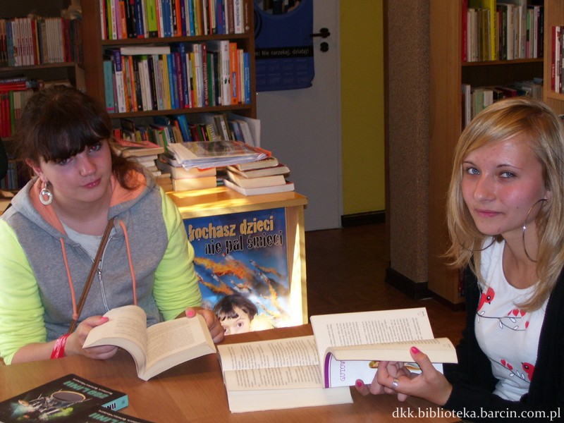 2 dziewczyny siedzące przy stoliku, trzymają w rękach otwarte książki