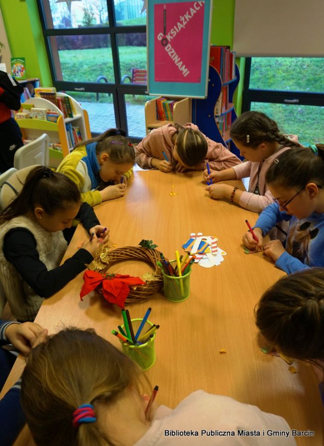 Grupa dziewczynek siedzących przy stole, każda z nich trzyma w ręku flamaster i coś nim koloruje lub pisze.