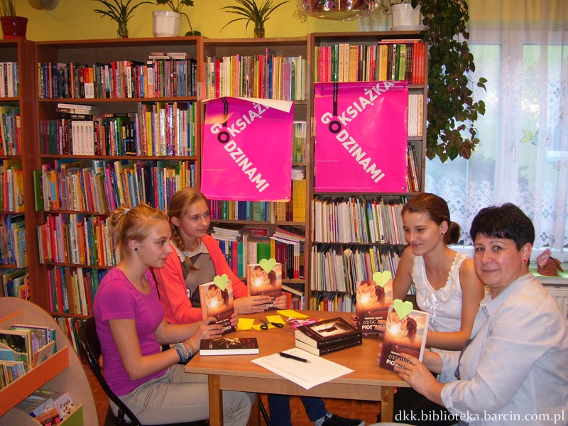 4 osoby, 3 uczestniczki i prowadząca spotkanie siedzą przy stole i pokazują do obiektywu aparatu książki z przyczepionymi żółtymi serduszkami