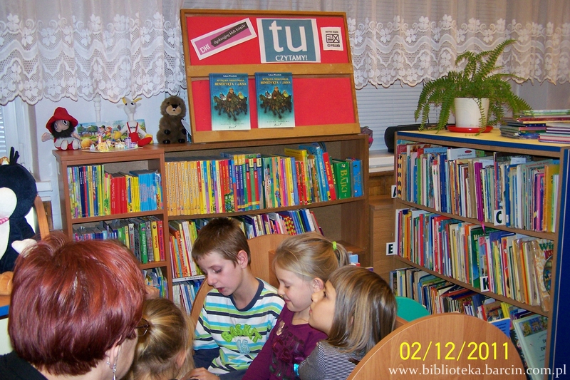 dzieci i prowadząca spotkanie bibliotekarka oglądają książki