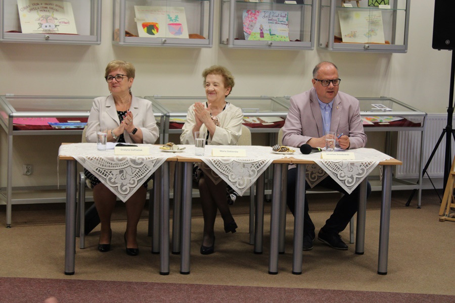 Jury konkursowe, trzy osoby (2 kobiety i mężczyzna) siedzą przy stolikach, uśmiechają się
