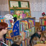 bibliotekarka prowadząca zajęcia pilnuje dzieci uczestniczące w spotkaniu które oglądają ksiązki.