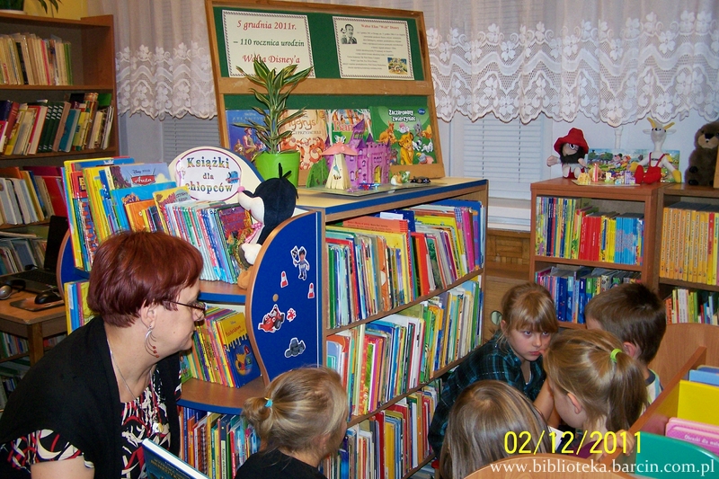 bibliotekarka prowadząca zajęcia pilnuje dzieci uczestniczące w spotkaniu które oglądają ksiązki.