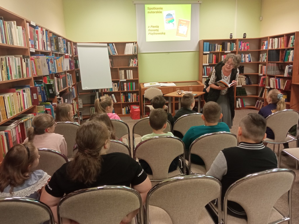 Zaproszona autorka książek przechadza się między zebranymi dziećmi i czyta fragment książki.