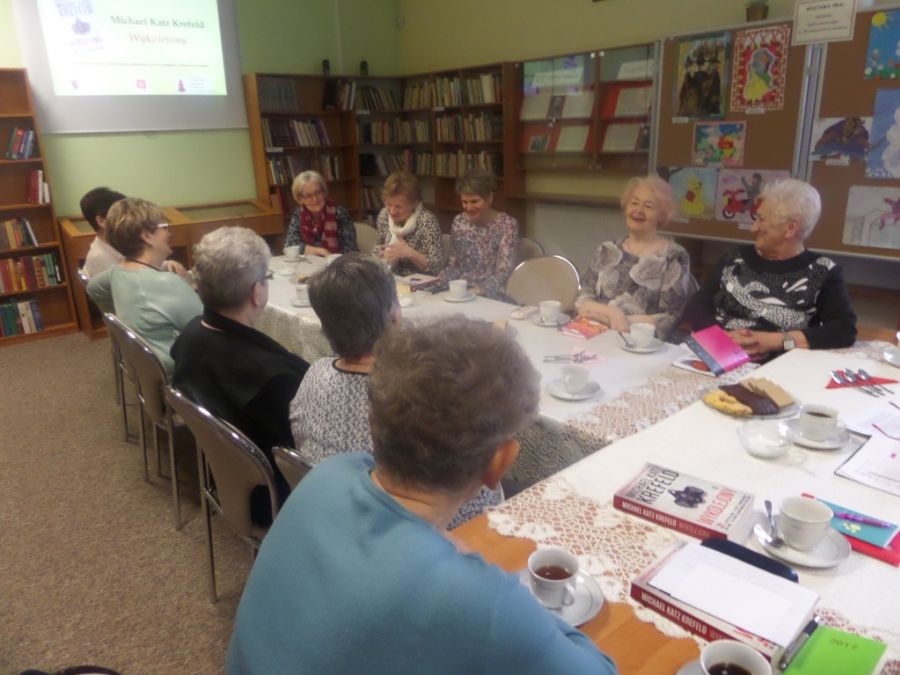 10 uczestniczek spotkania siedzi przy stołach ustawionych w literę T, z uśmiechami na twarzach rozmawiają między sobą