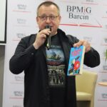 Marcin Przewoźniak, w jednej ręce trzyma mikrofon w drugiej książkę