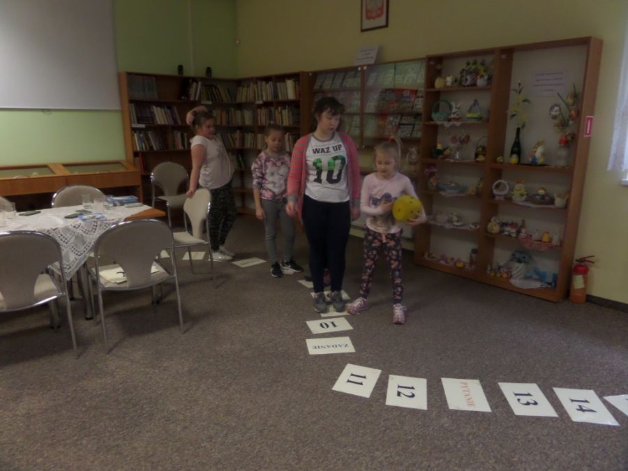 dzieci biorące udział w spotkaniu grają w grę złożoną ze ścieżki ułożónej z kartek papieru na niektórych kartkach pojawiają się takie napisy jak: "zadanie", "pytanie"