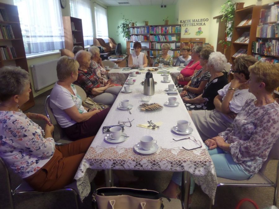 Na zdjęciu widać trzynaście osób, które brały udział w spotkaniu, wszyscy siedzą wzdłuż stołów ustawionych w literę "T"