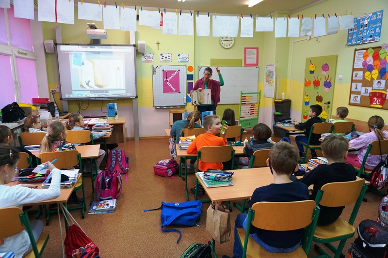 Zdjęcie sali lekcyjnej widać dzieci siedzące przy ławkach oraz Panią bibliotekarkę prowadzącą spotkanie Dyskusyjnego Klubu Książki