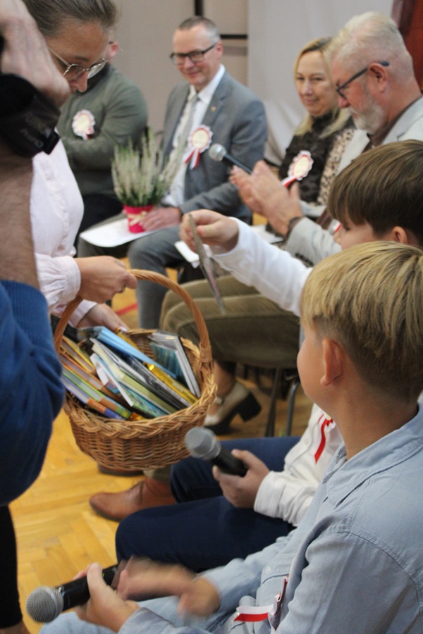 Pracownica biblioteki wręcza nagrodę osobie która poprawnie odpowiedziała na zadane pytanie