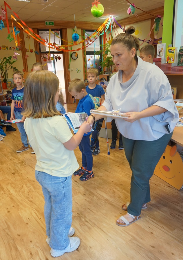 dziewczynka w białej koszulce i jasnoniebieskich dżinsach odbiera nagrodę za udział w konkursie