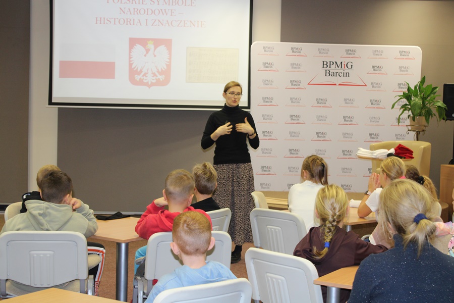 Prowadząca spotkanie bibliotekarka opowiada zebranym dzieciom o symbolach narodowych