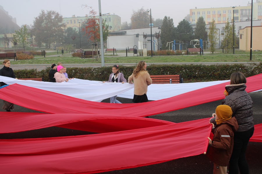 Grupa osób przed biblioteką rozciąga biało-czerwone płachty materiału